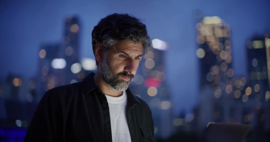 Light reflects on a mans face as he stands outside in a city