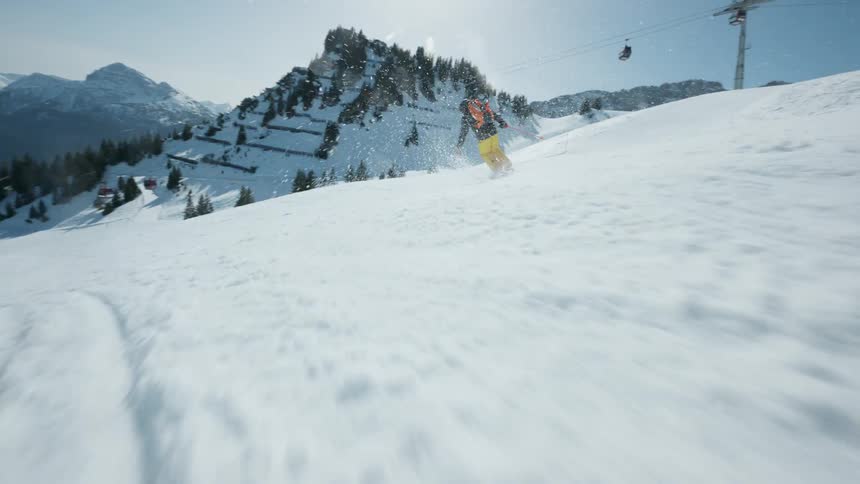 A skier descends a snowy slope on a bright sunny day with mountain views and a ski lift in the background