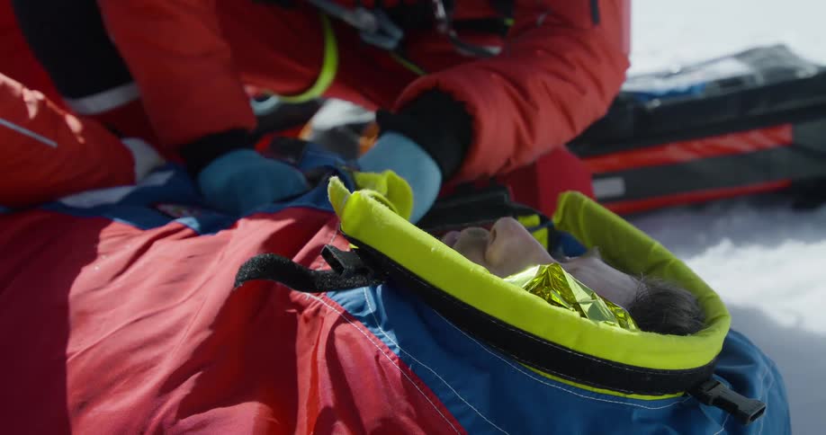 An injured man laying in the snow is getting help