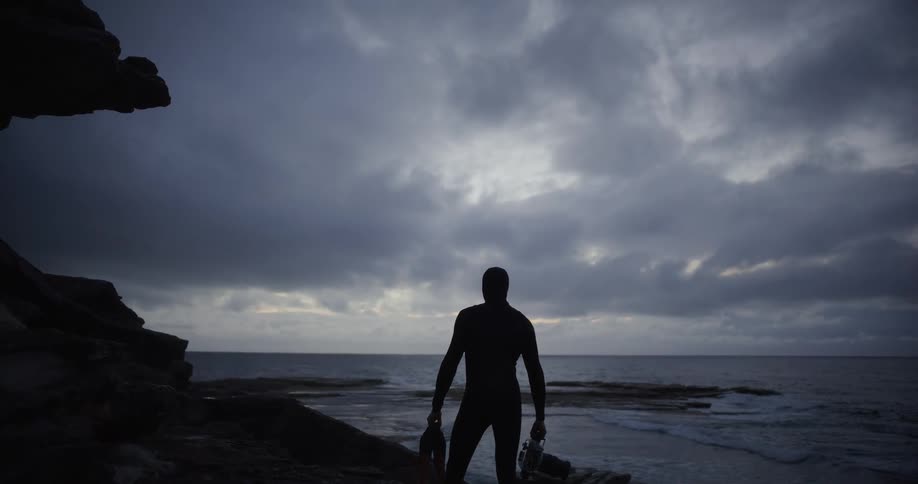The silhouette of a person standing in front of the sea with some waves breaking in the back at dusk