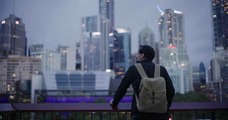 A man leans on his balcony looking at the tall buildings