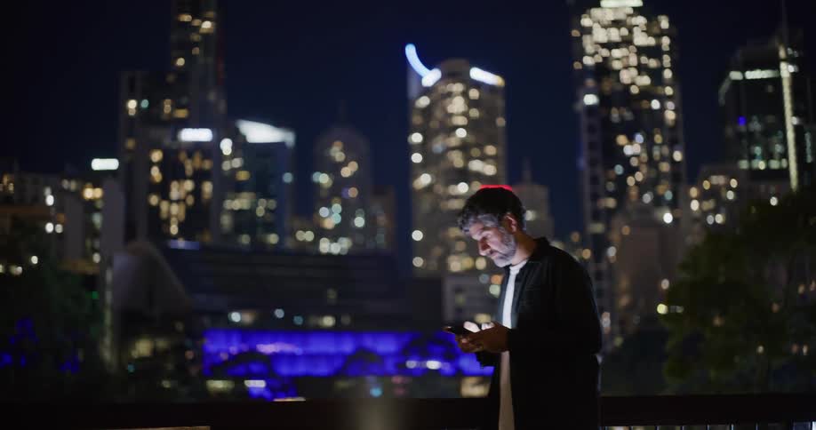 A man is using his cell phone with a skyline of tall buildings behind him