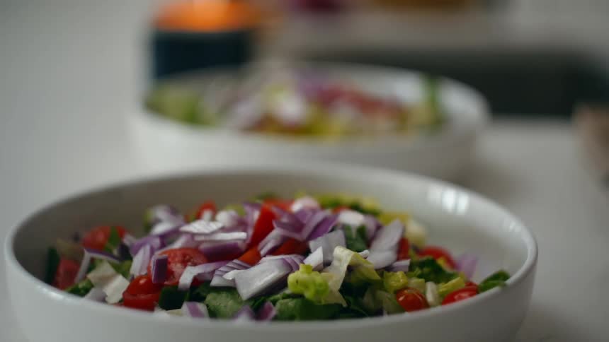 A bowls of salad with a sprinkling of red onions and cherry tomatoes sit on a white countertop
