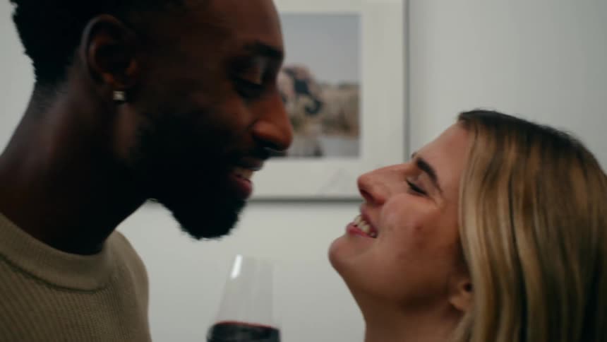 Couple clinks wine glasses and kisses while standing at home