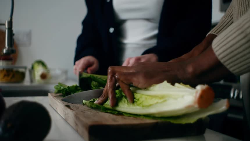 A man and woman are cutting lettuce in the kitchen