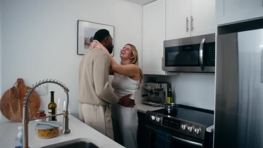A man and woman smile and kiss in the kitchen