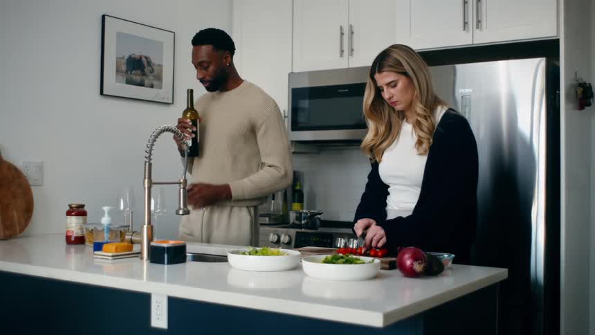 Man in the kitchen opening a wine and giving it to his wife next to him to smell it