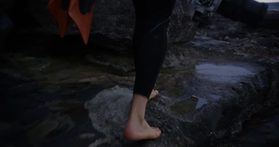 A person is climbing over the rocks on the shore while carrying a camera
