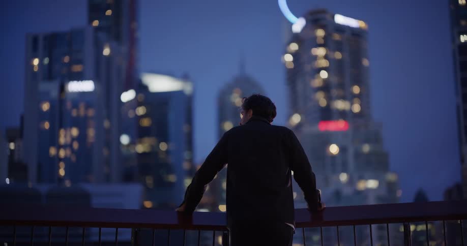A man is looking at the big city from the balcony