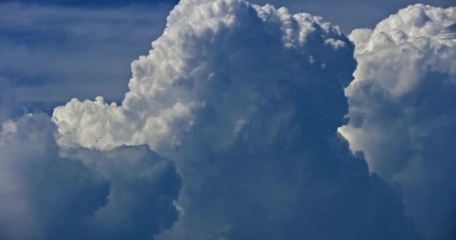 A close up view of large white billowing clouds moves against a blue sky