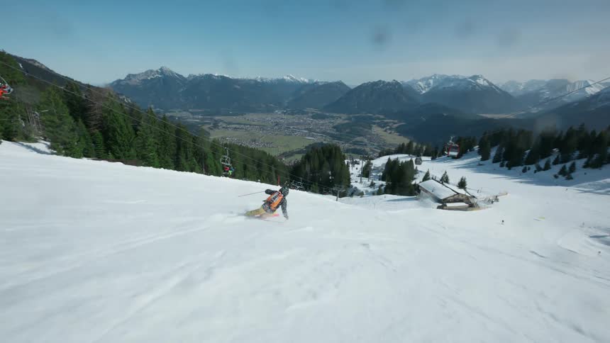 A skier with an orange backpack and yellow pants is skiing down a snowy mountain slope on a sunny day kicking up snow while making turns