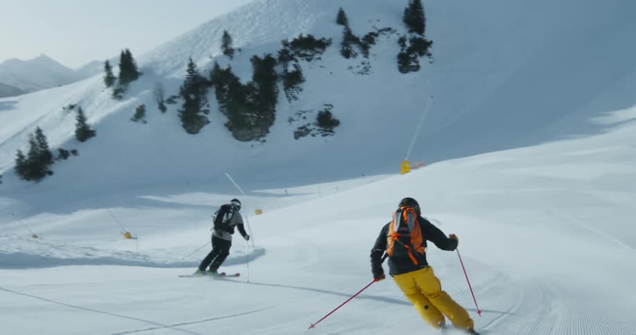 Two men ski down the long white slope on the mountain