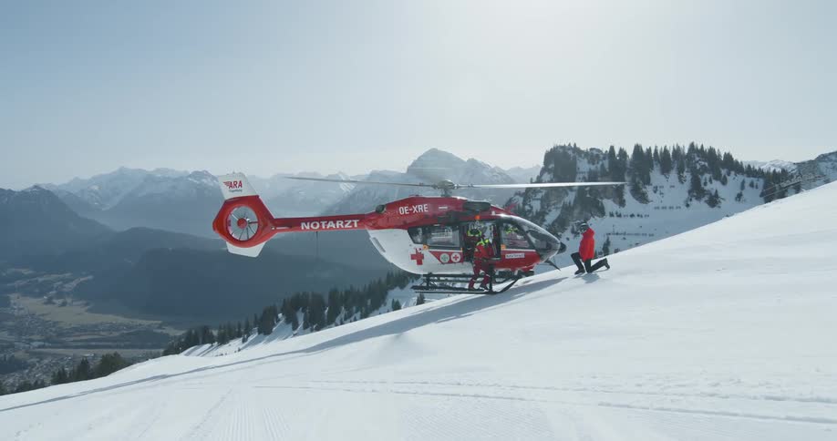 A rescue helicopter has landed on a snowy mountainside with personnel near the open door