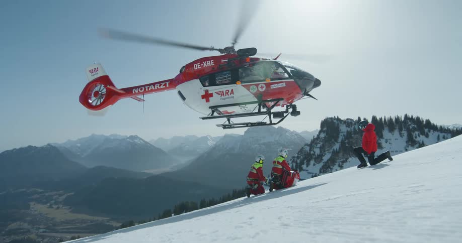 Helicopter taking off with rescuers on a snowy mountain