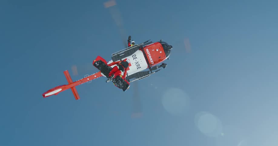 A rescue helicopter with a red cross symbol is flying in the sky carrying a person on a stretcher