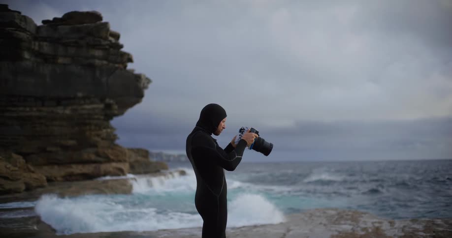Man standing up at the beach next to the coast photographing the ocean outdoors during day time