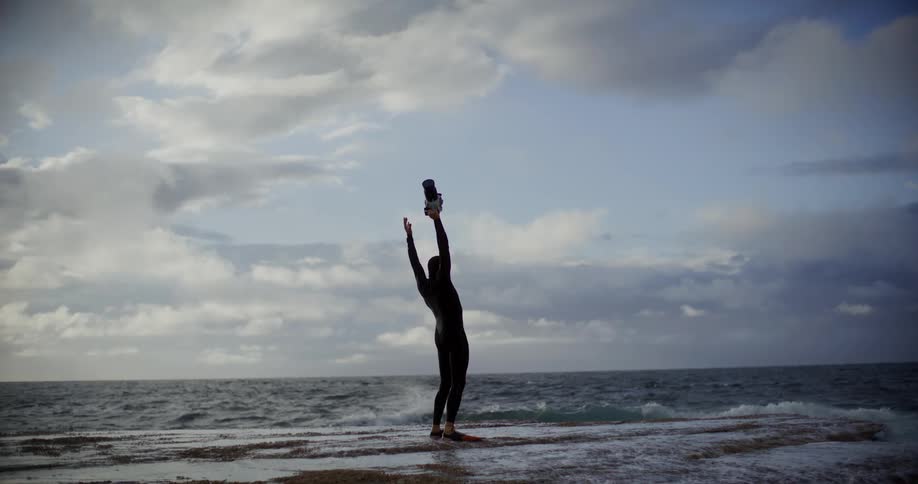A man raises his arms in the sky on the shore