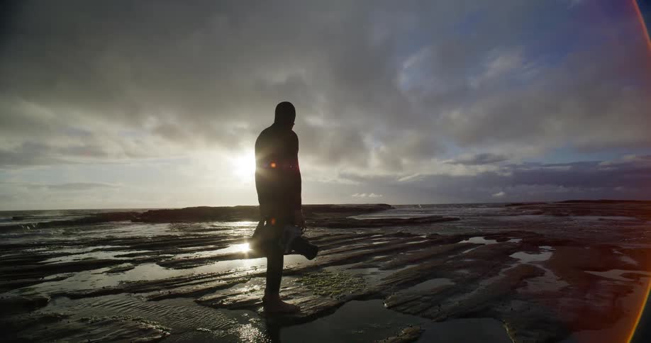 A man is standing in wet sand on a beach at sunrise