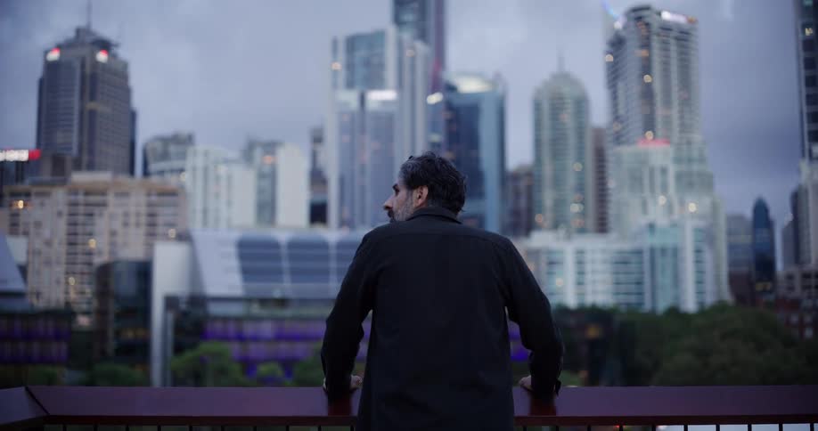 A person stands looking at a cityscape with modern highrise buildings under a cloudy sky