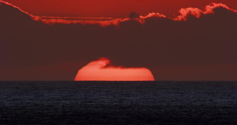Landscape of a calm and vast sea and in the background the sunrise with a reddish sky and clouds