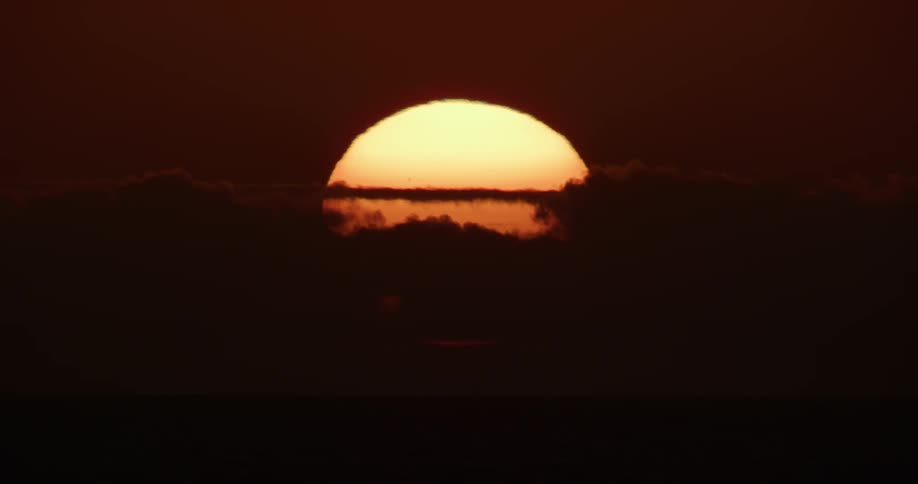 Sun covered by clouds over a dark flat land during dusk or dawn