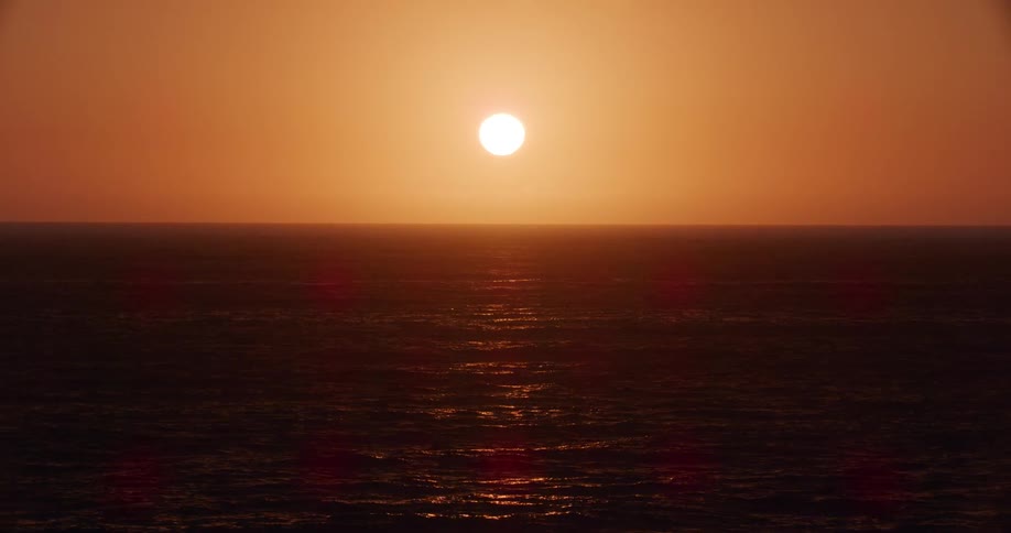Landscape of a calm sea against a reddish sky with the sun in the background