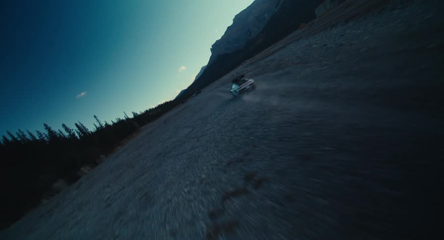 A car speeds down a dirt road in the mountains