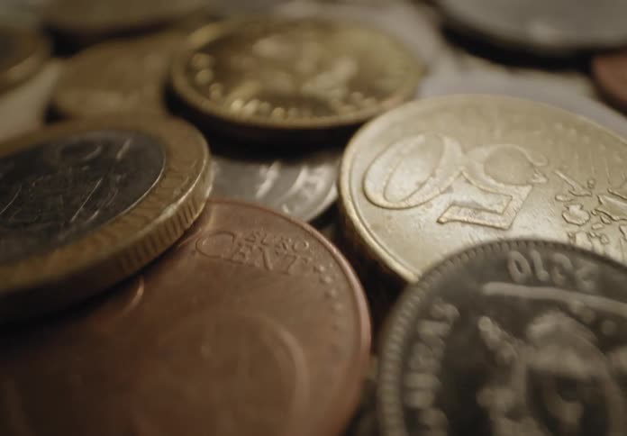 Several silver and bronze coins with faces drawn on their surface and underneath there are some banknotes