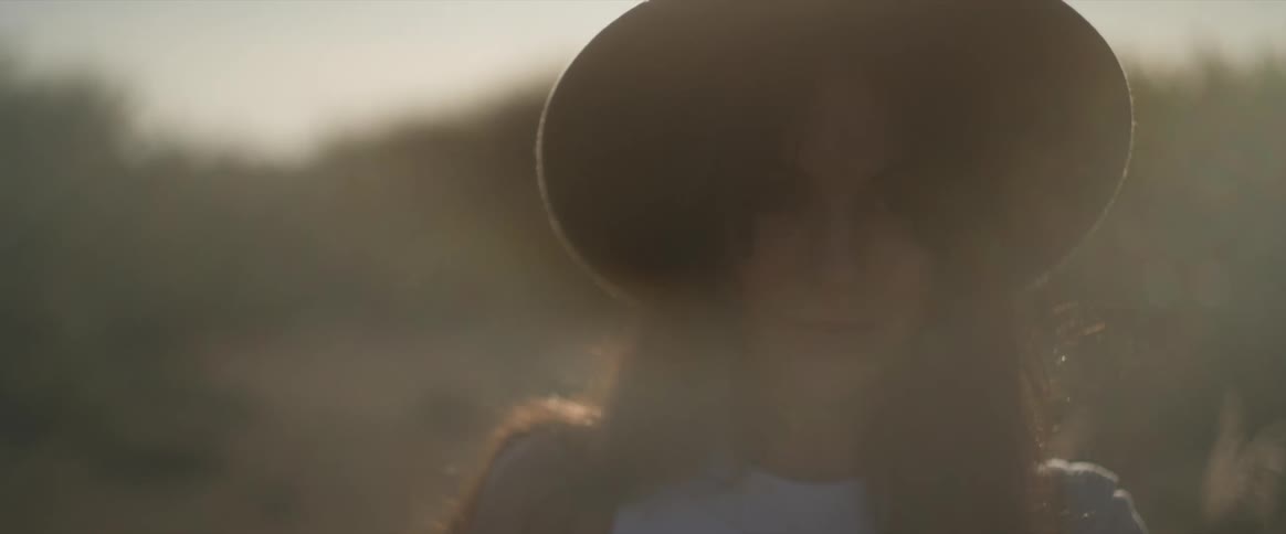 A woman wearing a widebrimmed hat is partially obscured by sunlight creating a soft warm glow around the figure