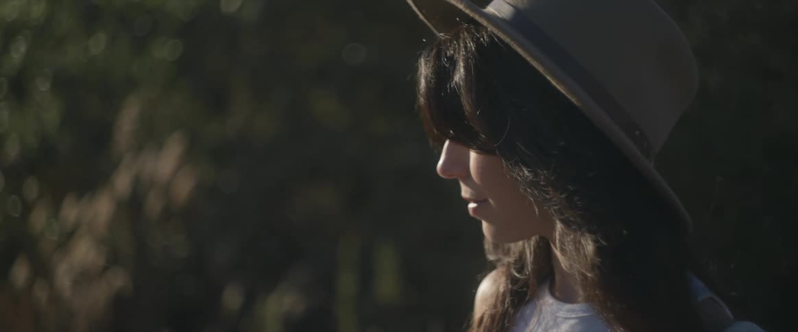 The face of a young woman wearing a hat and she is looking sideways on a clear day