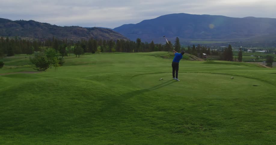 A person in a blue shirt is standing on a golf course after hitting a ball