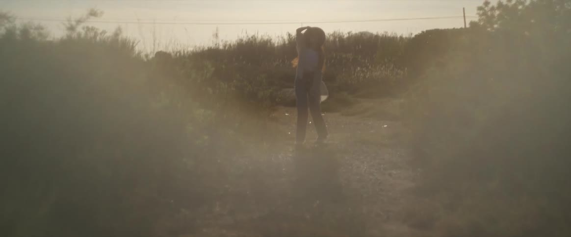 A silhouetted woman joyfully spins and puts on her hat in a sun drenched field