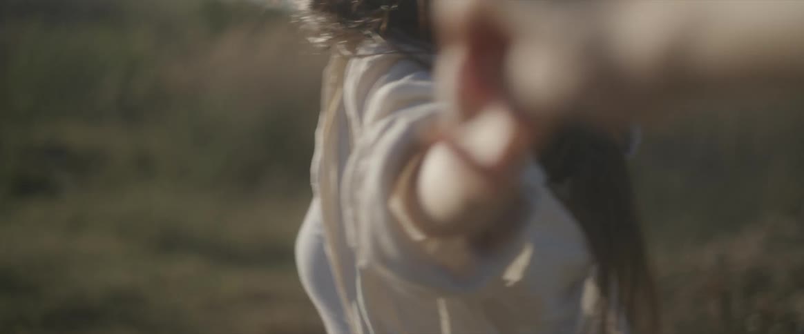 A woman wearing a hat smiles while holding another persons hand as they run in the countryside