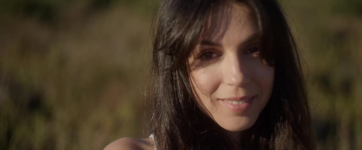 A woman with dark hair a neutral expression and some shadows on her face