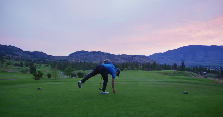 A man playing on a golf course with mountains and a colorful sunset sky in the background