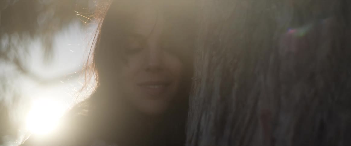 Portrait of a young woman with a happy facial expression leaning her face against a tree outdoors