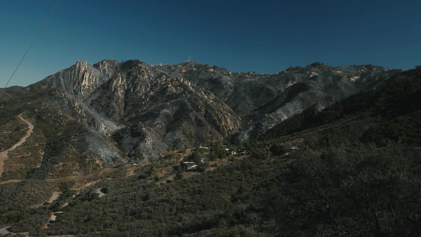 Rocky mountains with steep slopes show dark burn scars under a clear blue sky