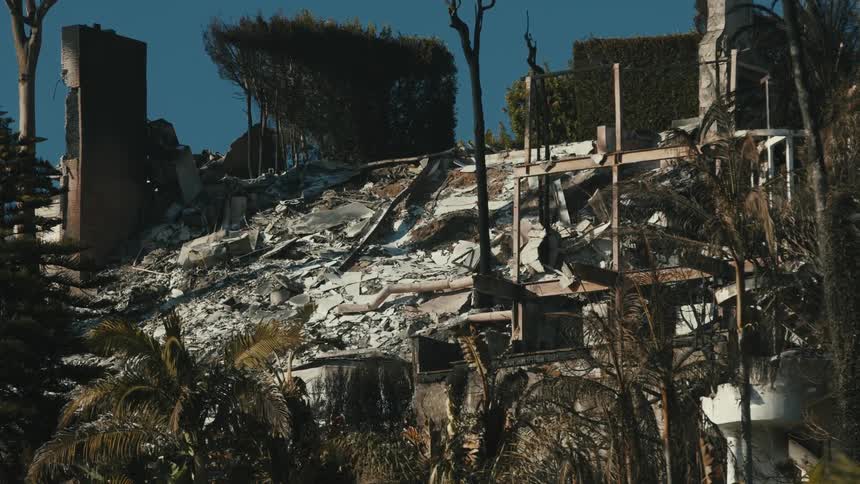 A destroyed building with several piles of rubble and some vegetation around it on a blue day