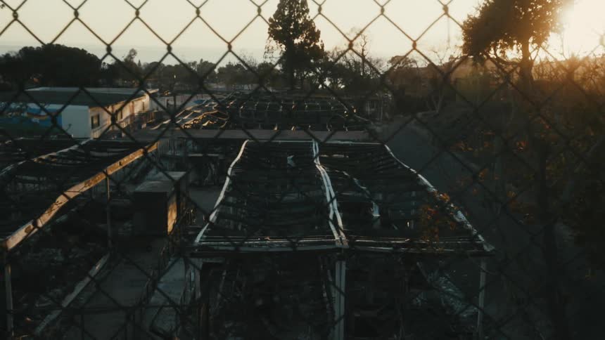 A view through a metal fence of some destroyed and burned buildings