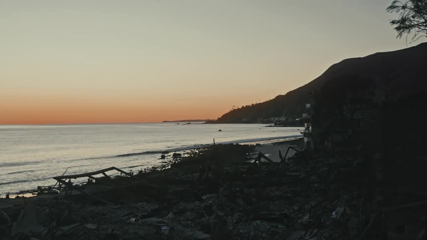 The aftermath of a disaster a fire on a beach at sunset showing the destruction of buildings and debris against a calm ocean and hillside