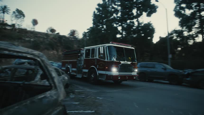 A firetruck moves down a street with burned vehicles on the side