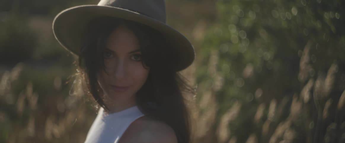 A young woman models a hat and clothing in a grassy field