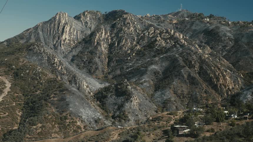 Charred mountain towers over nearby rural buildings under a blue sky