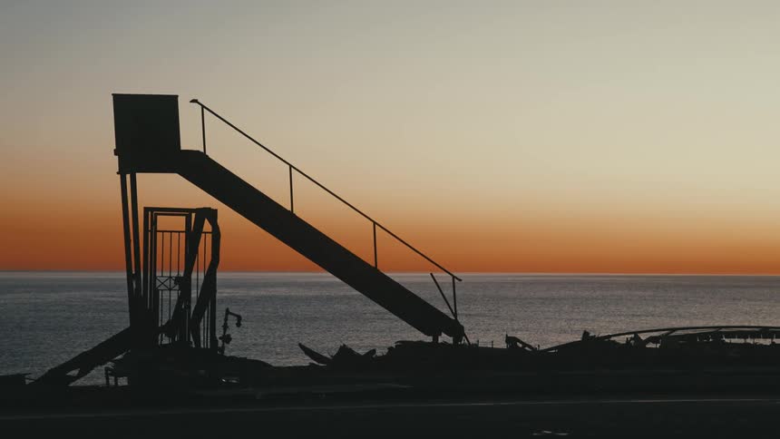 A lifeguard stand sits on a beach with the ocean and sunset behind it