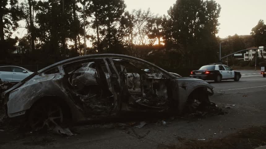 Traffic passes by an accident with a burned car