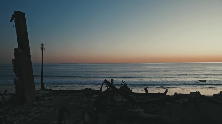 Dark ruins contrast with the serene horizon where the calm sea reflects warm tones of the sunset