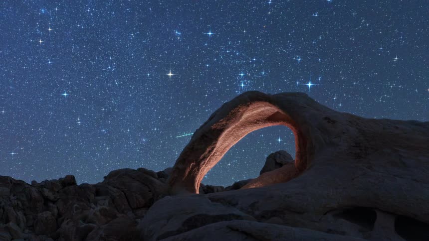 Stone arch illuminated by a warm light under a starry sky