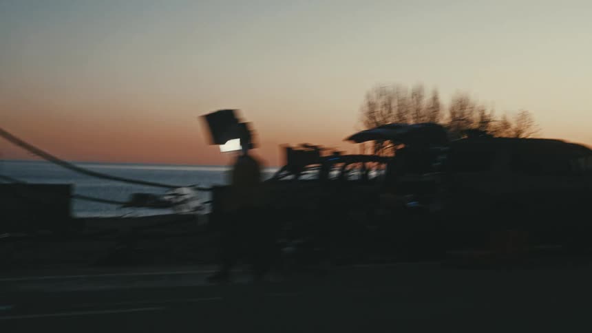 Moving view of a road with vehicle traffic and in the background a sea against a reddish sky