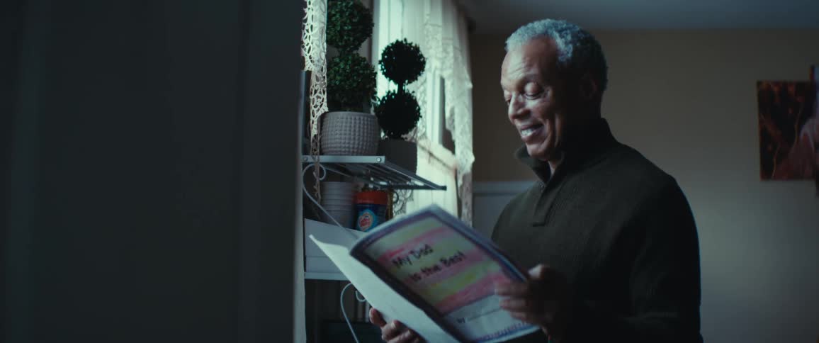Older man smiles while standing and looking at a booklet made by a son for his father