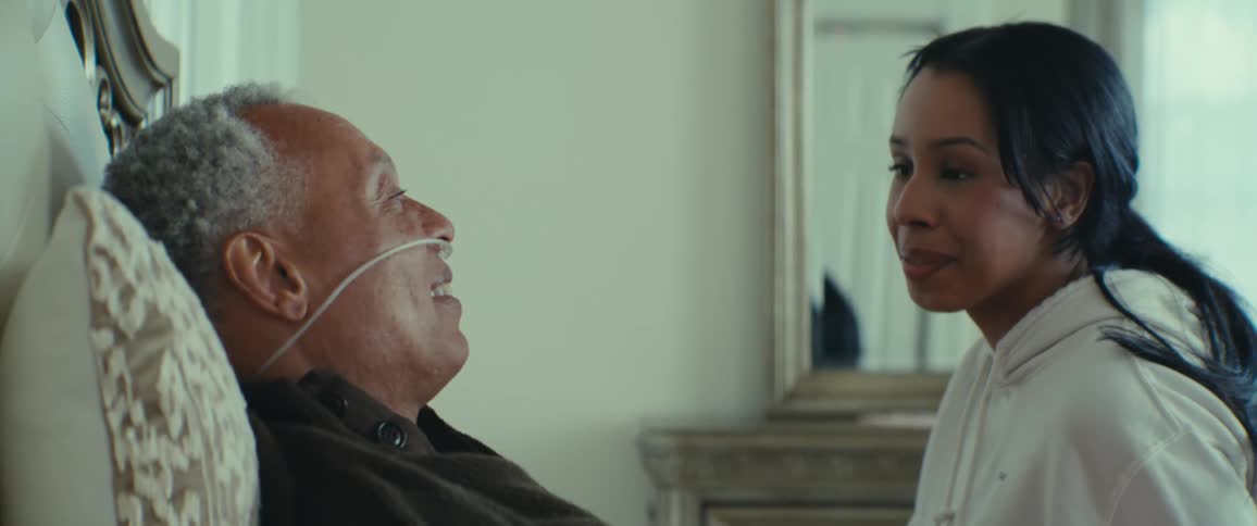 Daughter sitting on bed talking to her elderly father who is using an oxygen catheter in his nose